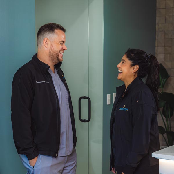 Dr. Quintana and Dr. DeMarco smiling in black jackets chatting in a clinic in Dripping Springs, TX