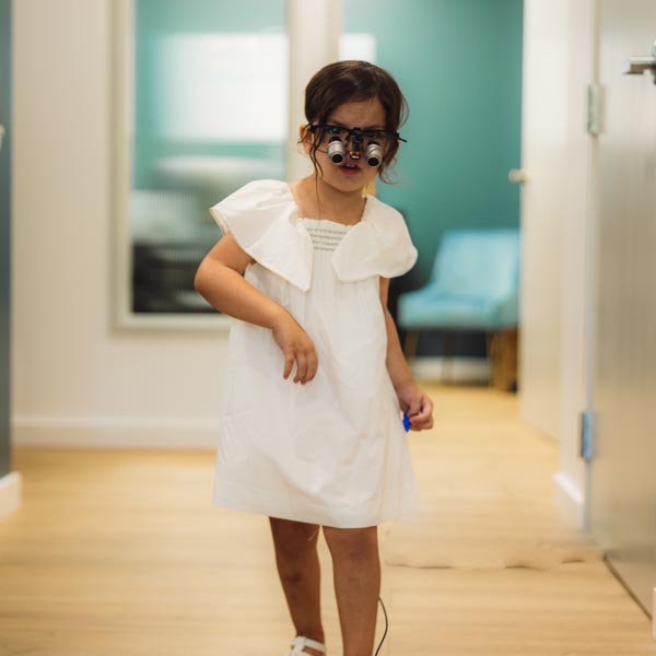 Young girl in white dress wearing binocular glasses indoors in Dripping Springs, TX